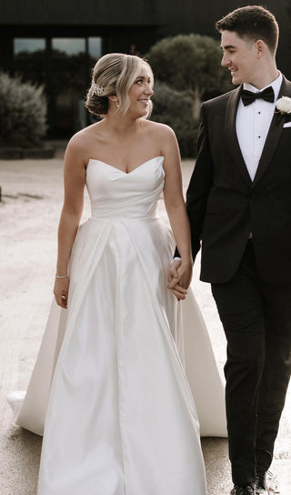 Classic white bridal gown with a structured strapless bodice and soft pleated detailing, featuring a flowing full skirt for a romantic wedding day aesthetic.