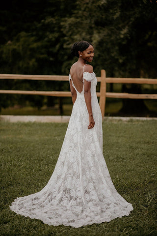 Feminine lace bridal gown with soft spaghetti straps, a scalloped lace train, and floral motifs, perfect for intimate and outdoor weddings.