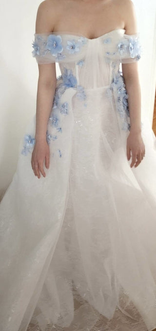 Chic bridal or event dress with a sheer bodice, delicate blue floral accents, and a flowing shimmering skirt, perfect for whimsical celebrations or elegant themed parties