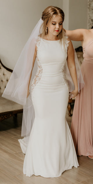 Modern and chic wedding dress with a bateau neckline, lace-adorned sides, and a tailored silhouette, perfect for brides seeking understated elegance with delicate details