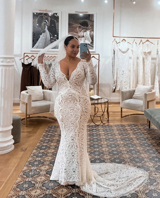 Elegant long-sleeve wedding gown with intricate lace detailing, plunging V-neckline, and a fitted silhouette that flows into a dramatic chapel train, perfect for classic and romantic ceremonies