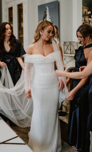 Sophisticated ivory bridal gown adorned with sequins, sheer lace off-the-shoulder sleeves, and a fitted floor-length design, designed for modern and luxurious wedding aesthetics