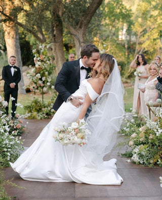 Chic ivory satin wedding gown with off-the-shoulder detailing, a figure-flattering mermaid silhouette, and a flowing train, tailored for glamorous and romantic bridal looks