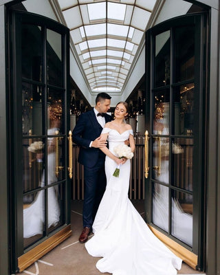 Elegant off-the-shoulder bridal dress featuring a structured bodice, sleek mermaid fit, and dramatic floor-length train, ideal for sophisticated and modern weddings