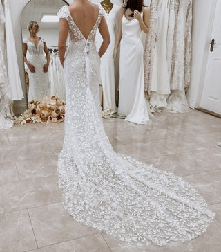 Chic ivory mermaid gown with floral lace applique, deep V-neckline, short cap sleeves, and a backless fit-and-flare silhouette, tailored for boho-inspired and beach weddings