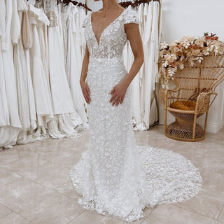 Custom ivory mermaid bridal gown with 3D floral lace applique, deep V-neckline, short cap sleeves, backless design, and fit-and-flare silhouette, perfect for boho beach weddings