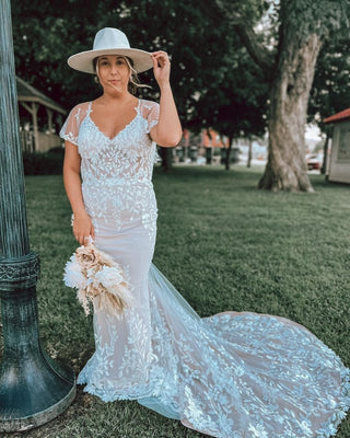 Bohemian lace wedding dress with a sheer overlay and intricate floral embroidery, paired with a wide-brim hat for a rustic chic bridal look