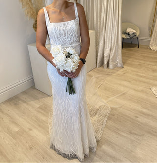 Modern bridal dress with a fitted bodice and intricate embroidery, minimalist square neckline, sleeveless design, and a sleek train, ideal for a stylish and understated wedding theme