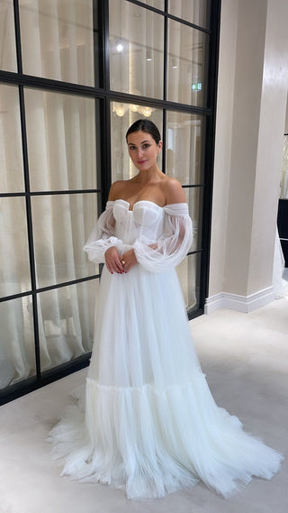 Romantic off-the-shoulder bridal gown with sheer tulle puff sleeves, a structured corset bodice, and a flowing A-line skirt, perfect for whimsical and modern wedding styles