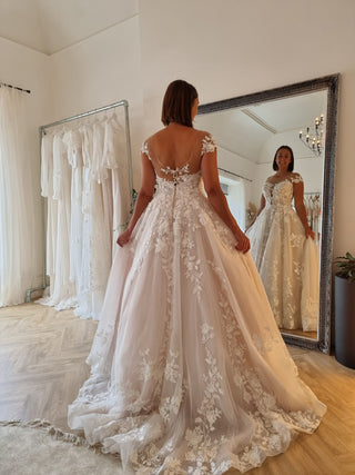 Custom white bridal gown featuring delicate floral lace detailing, strapless sweetheart neckline, and flowing A-line tulle skirt, ideal for fairytale-inspired wedding celebrations