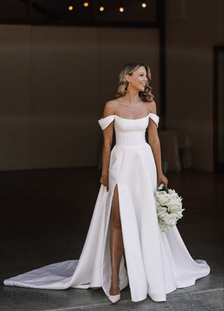 Romantic off-the-shoulder wedding gown with a thigh-high slit and dramatic train, ideal for a modern bride