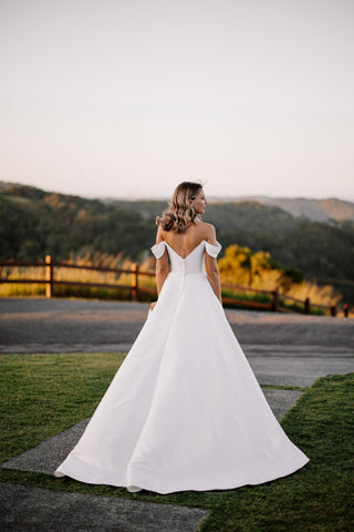 Chic white wedding dress with a structured silhouette, off-the-shoulder neckline, and long train, paired with classic heels