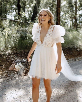 Whimsical short white wedding dress featuring a plunging V-neckline, floral appliqués on the bodice, and voluminous puff sleeves with dotted tulle, perfect for outdoor or bohemian-inspired ceremonies