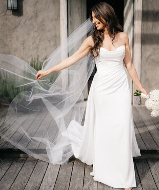 Elegant strapless ivory wedding gown with a sweetheart neckline, draped bodice, and sleek floor-length silhouette, complemented by a flowing veil, perfect for timeless bridal looks