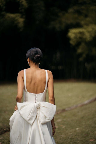 Elegant minimalist wedding gown with a deep open back, delicate straps, and a statement oversized bow, styled for an outdoor ceremony