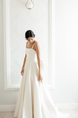 Sophisticated bridal dress featuring a sleek A-line silhouette, plunging open back, and a dramatic bow detail, perfect for modern weddings