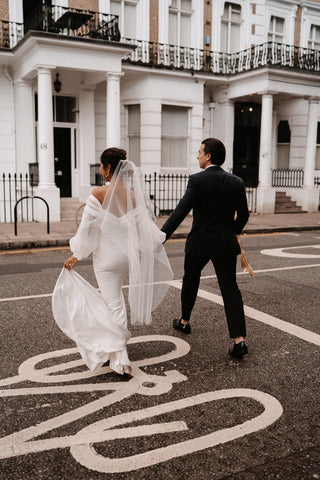 Chic bridal dress featuring an off-the-shoulder neckline with draped fabric, complemented by ethereal sheer sleeves and a sleek, figure-hugging design