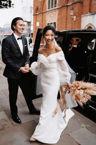 Modern off-the-shoulder wedding gown with sheer billowing sleeves and a fitted silhouette, exuding elegance and contemporary style