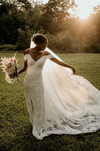 Elegant lace wedding dress with a fitted silhouette, off-the-shoulder accents, and a dramatic slit, designed for a chic and stylish bride.

