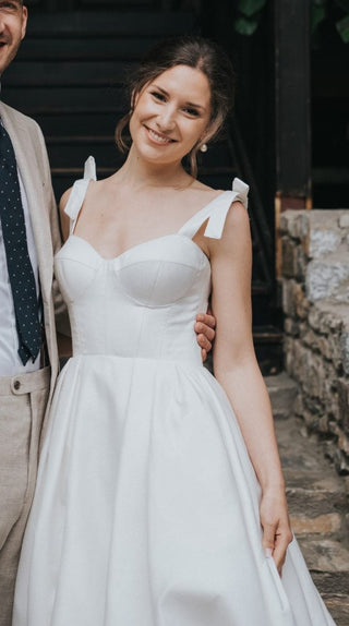 Modern yet traditional wedding dress with a fitted bodice, feminine bow-tied straps, and a voluminous A-line skirt for a sophisticated bridal silhouette.