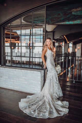 Timeless bridal gown with a fitted silhouette, corset-inspired bodice, intricate floral lace embroidery, and a dramatic train, styled with a cascading bouquet, perfect for elegant indoor ceremonies