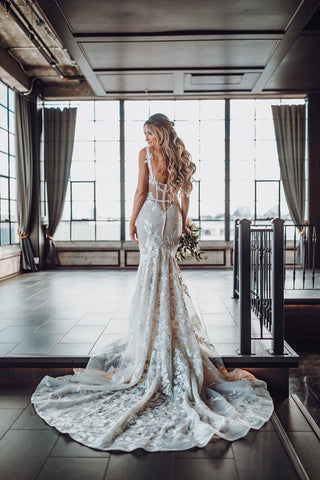 Romantic wedding gown with a figure-hugging design, floral lace accents, and a structured bodice with sheer paneling, complemented by a dramatic train and veil, perfect for modern brides