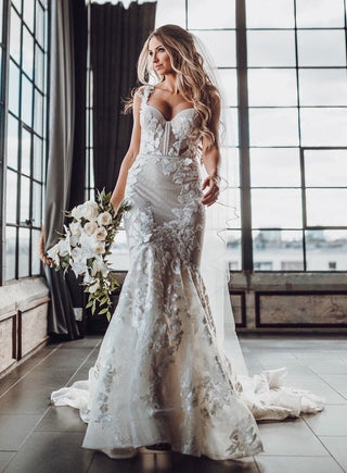 Elegant mermaid wedding gown with intricate floral lace detailing, a sheer corset bodice, and a dramatic sweetheart neckline, paired with a flowing chapel train and veil, perfect for luxurious indoor ceremonies