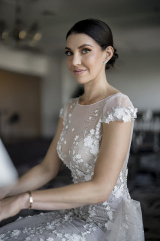 Timeless bridal dress featuring delicate lace flowers, fitted silhouette with a floor-length train, cap sleeves, and sheer overlay, perfect for romantic outdoor ceremonies, complemented by the groom's crisp white dinner jacket