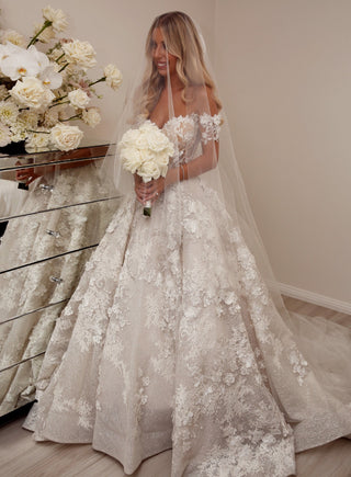 Custom ivory ball gown with 3D floral lace applique, sparkly sequin detailing, sweetheart neckline, and off-the-shoulder puff sleeves, floor-length A-line design perfect for fairytale princess weddings