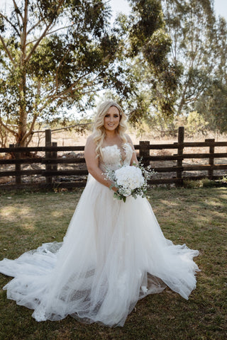 Sophisticated ivory tulle ball gown, adorned with intricate 3D floral details, off-the-shoulder puff sleeves, a deep V-plunge neckline, and high slit, perfect for fairy-tale inspired weddings