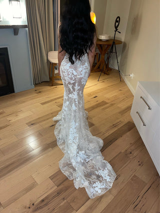 Romantic mermaid-style wedding dress adorned with floral lace motifs, a plunging V-neckline, and shimmering tulle layers, designed to create a dramatic yet elegant statement