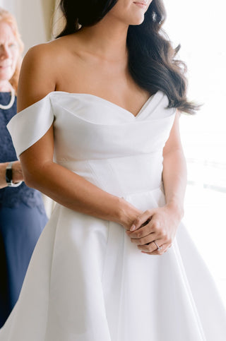 Elegant white wedding dress crafted in luxurious satin, complete with a structured off-the-shoulder neckline and flowing train for a statement look