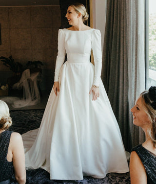 This elegant white bridal gown features a timeless A-line silhouette, designed to create a refined and graceful look for the modern bride. The full-length sleeves, paired with the structured, puffed shoulders, offer a sophisticated vintage vibe. The classic scoop neckline and smooth satin fabric enhance the gown's luxurious feel, making it an ideal choice for a chic, formal wedding.