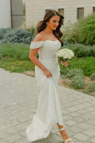 Sparkling off-shoulder bridal gown with a form-fitting silhouette and delicate bead detailing, perfect for a modern bride seeking a glamorous look.