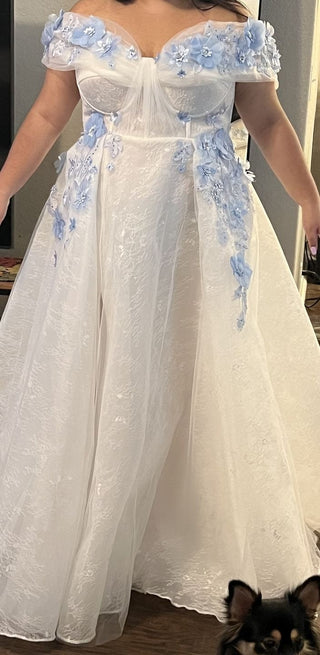 Elegant white and blue ballgown with hand-applied 3D flowers, an off-the-shoulder neckline, and a shimmering tulle overlay, ideal for dreamy weddings or fairy-tale occasions