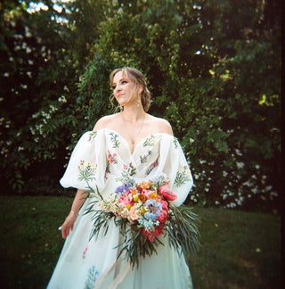 Off-shoulder gown with delicate floral embroidery on a flowing white fabric, adding a romantic and airy feel to the look.