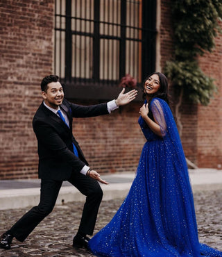 Sophisticated cobalt blue glitter gown, adorned with gold celestial stars, long cape sleeves, sweetheart neckline, and A-line floor-length design, suitable for proms, weddings, and evening galas