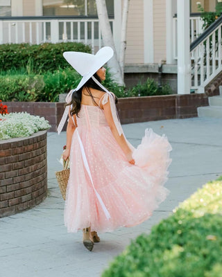 Chic light pink tea-length dress with shimmering tulle layers, thin straps, and a flattering A-line silhouette, paired with a white cowboy hat for a unique bridal or event look