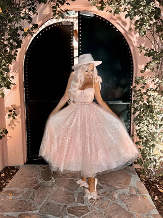 Light pink glitter tulle tea-length dress with a sweetheart neckline, thin straps, and a voluminous A-line silhouette, accessorised with a white cowboy hat, perfect for whimsical weddings and romantic celebrations