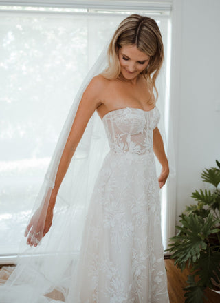 This strapless wedding gown features a corset-style bodice with intricate floral lace appliqués

The delicate sheer detailing adds a modern