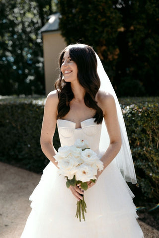 Romantic strapless wedding gown featuring a structured corset bodice and layered tulle skirt, paired with a classic bridal veil for timeless elegance.