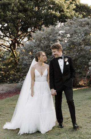 Whimsical bridal dress with a layered tulle skirt, fitted bodice with a deep neckline, and lightweight straps, ideal for modern brides seeking an ethereal and chic look