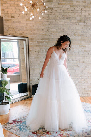 Romantic white tulle ballgown featuring a plunging V-neckline, delicate spaghetti straps, and a tiered flowing skirt, perfect for timeless and elegant wedding ceremonies