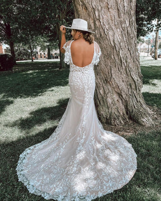 Modern bridal gown featuring a form-fitting silhouette, delicate floral lace details, and a dramatic train for countryside weddings,