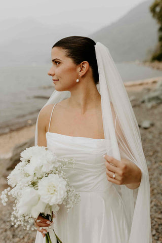 Elegant minimalist wedding dress with a ruched bodice and thin straps, complemented by a flowing veil, perfect for beachside or lakeside ceremonies.