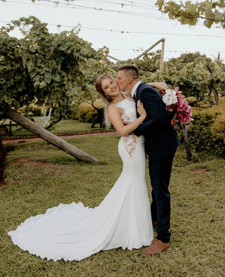 Modern and chic wedding dress with a bateau neckline, lace-adorned sides, and a tailored silhouette, perfect for brides seeking understated elegance with delicate details