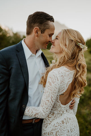 Timeless white lace gown with full-length sleeves, a plunging neckline, and a curve-enhancing silhouette, finished with a flowing train, perfect for modern brides seeking a romantic and chic look