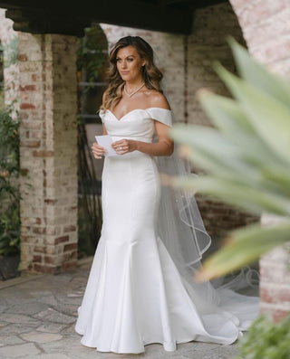 Ivory off-the-shoulder mermaid wedding gown with a fitted silhouette, sweeping train, and classic satin fabric, perfect for elegant and timeless bridal celebrations