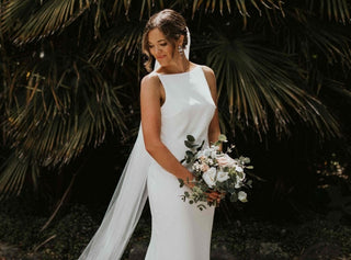 Elegant ivory wedding gown with a high bateau neckline, fitted silhouette, and floor-length train, perfect for modern and minimalist bridal styles