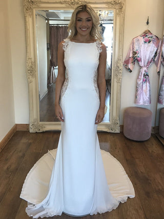 Elegant sheath-style wedding gown with a high bateau neckline, intricate lace side detailing, and a flowing chapel train, perfect for sophisticated and modern bridal looks